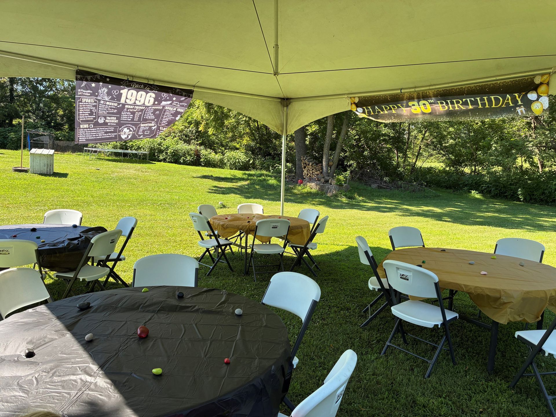 Outdoor tent with round tables and chairs under a canopy, beside a grassy hillside with flowers.