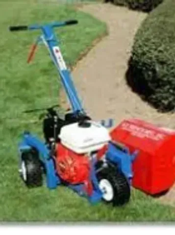 Blue and red lawn edger with gas engine, edging a lawn next to a sidewalk.