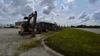 Construction equipment parked on gravel next to a grassy area under a cloudy sky.