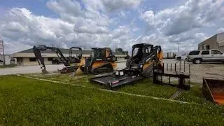 Construction equipment on grass near buildings under a cloudy sky.