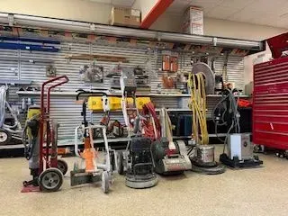 Tools lined up in a hardware store. Red, black, and yellow equipment on a tile floor with shelves in the background.