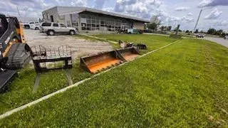 Construction equipment on a grassy lawn in front of a commercial building on a cloudy day.