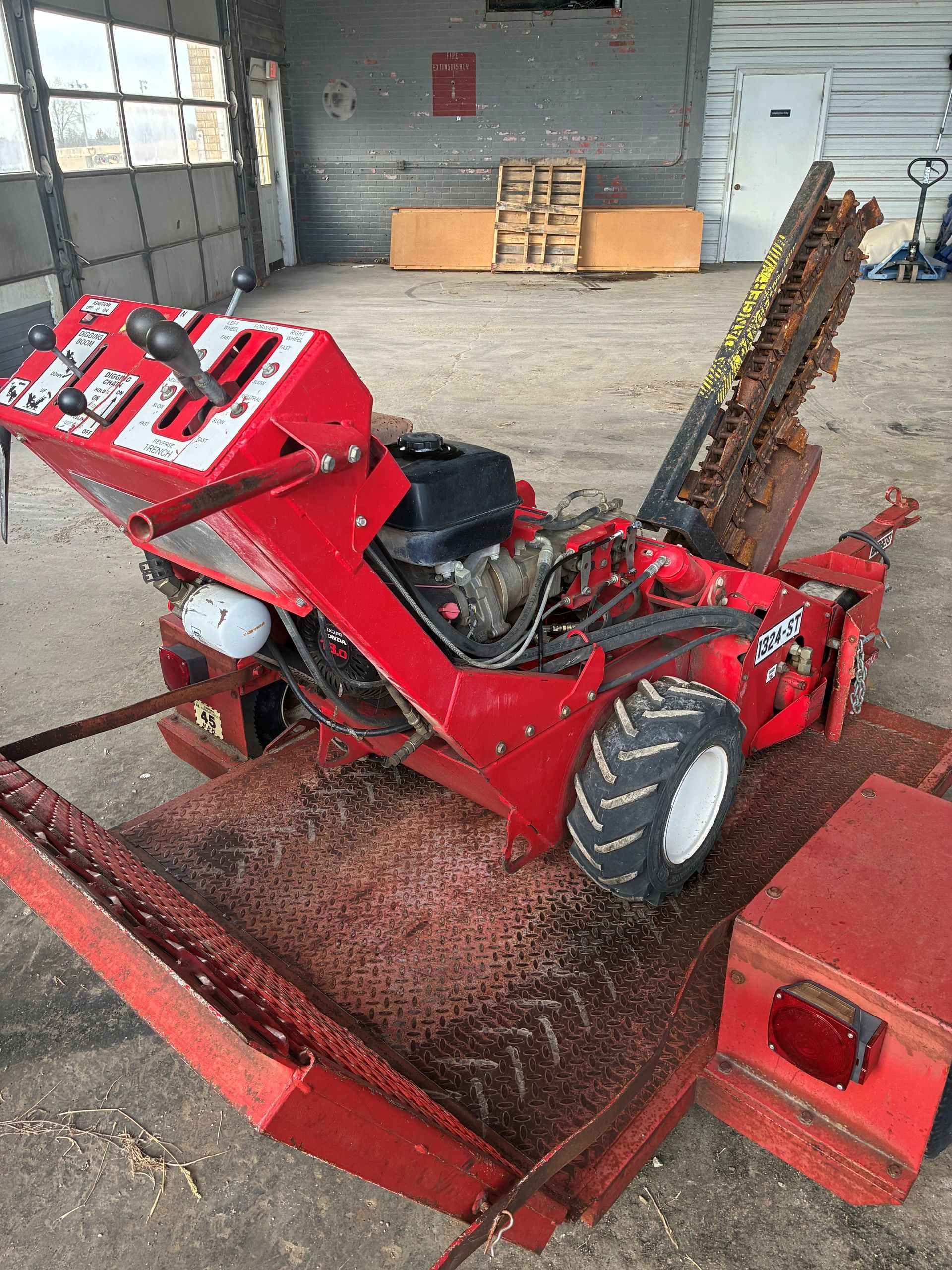 Red trencher machine with black engine, parked on a metal platform, indoors.