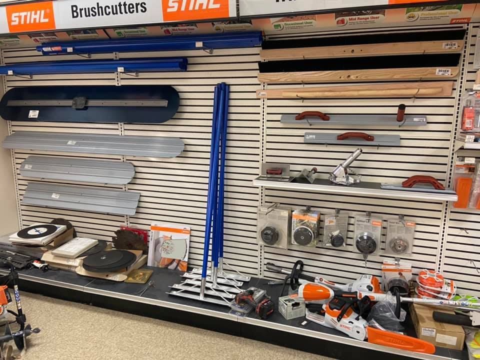 Tools displayed on a store wall, including concrete floats, handles, and saw blades.