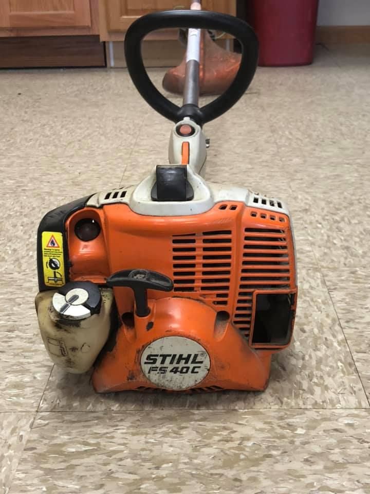 Stihl FS 40 C orange and white string trimmer on a tiled floor, with a black handle and red trash can in the background.
