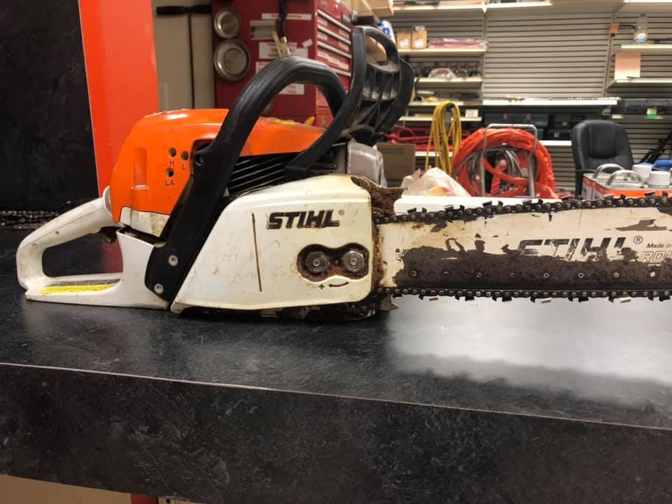 STIHL chainsaw on a dark workbench, white and orange with a dirty blade.