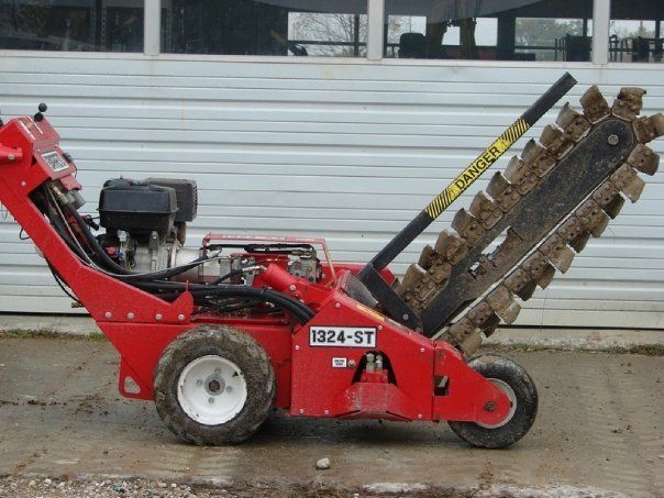Red trenching machine digging a trench in front of a building.