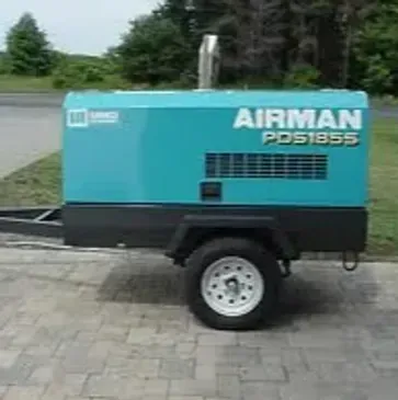 A turquoise Airman PDS185S air compressor on a black trailer, parked outside.