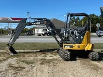 John Deere 35G mini excavator in yellow and black on a gravel surface with a blurred background.