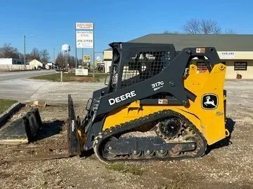 Yellow and black John Deere 317G compact track loader with tracks, parked outdoors.