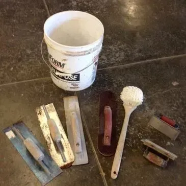 Bucket and several trowels and brush on a cement floor; tools for construction or craftwork.
