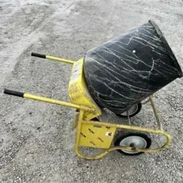 Yellow wheelbarrow cement mixer on a gravel surface. Black drum, two wheels, and handles.