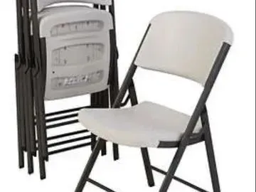 White folding chairs stacked and open, with black metal frames, indoors.