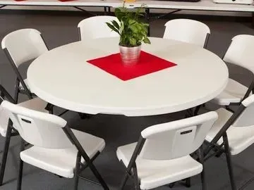 Round white table with white folding chairs, red square centerpiece, potted plant.