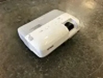 White and grey projector on a dark, textured surface, viewed from an angle.