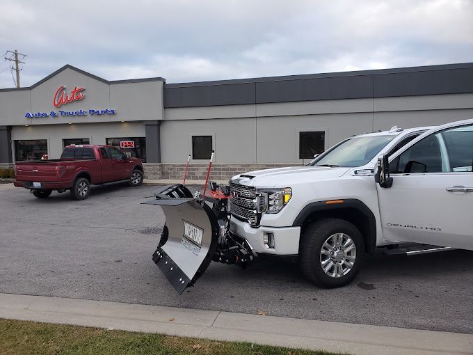 A white truck with a snow plow attached to it is parked in front of a building.
