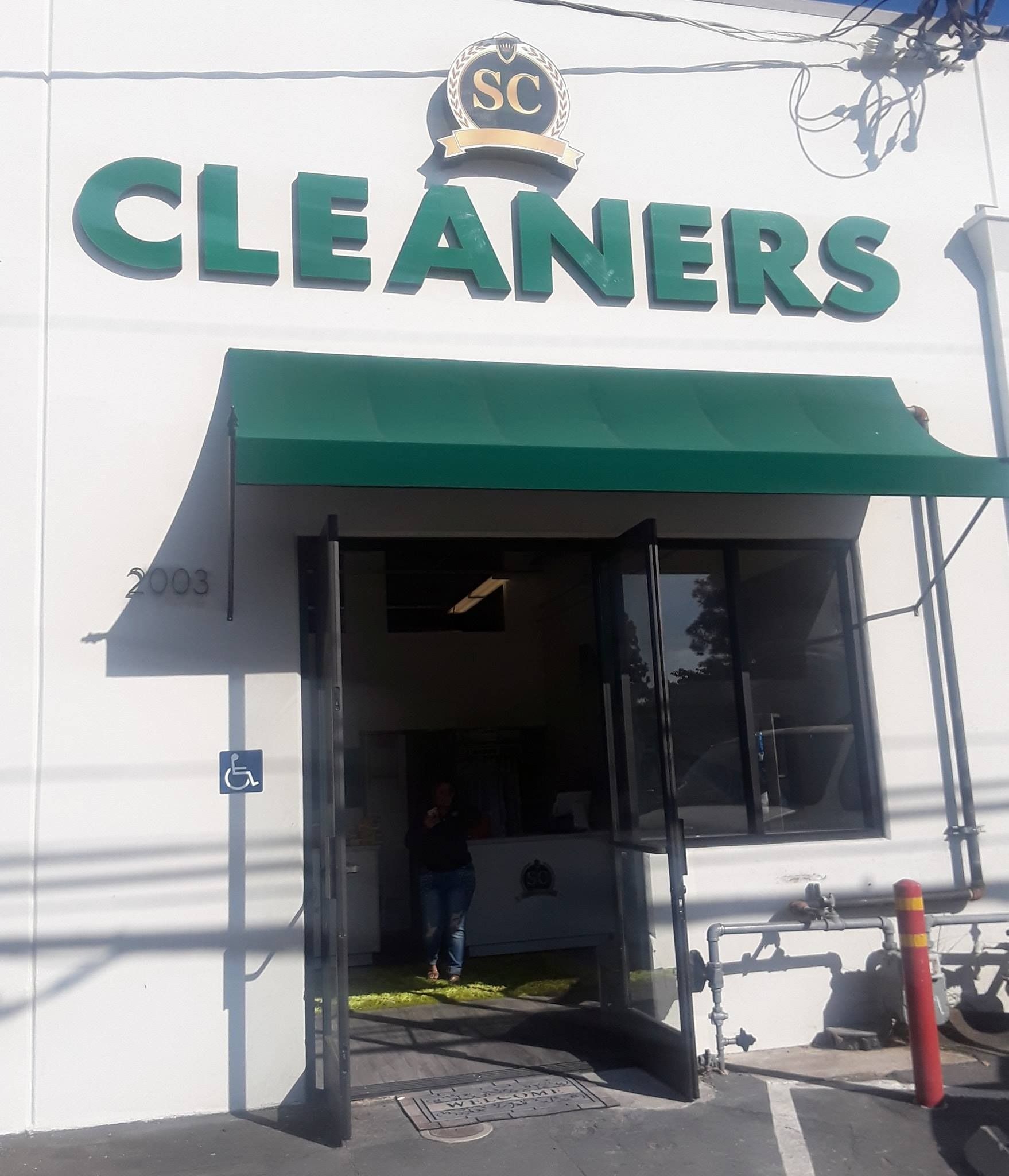 Storefront of a cleaners shop with a green awning and large “CLEANERS” sign.