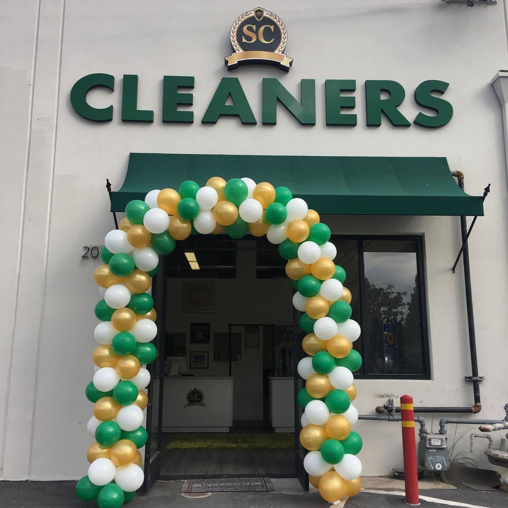 Storefront of a cleaners with a green-and-white balloon arch around the entrance