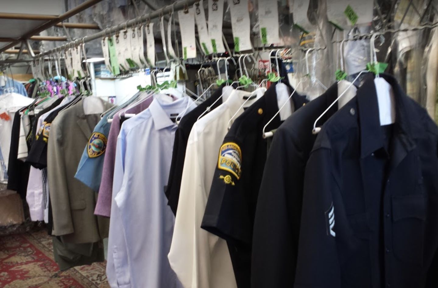 Clothes hanging on a rack outdoors under a canopy, including shirts and jackets in white, navy, and beige.
