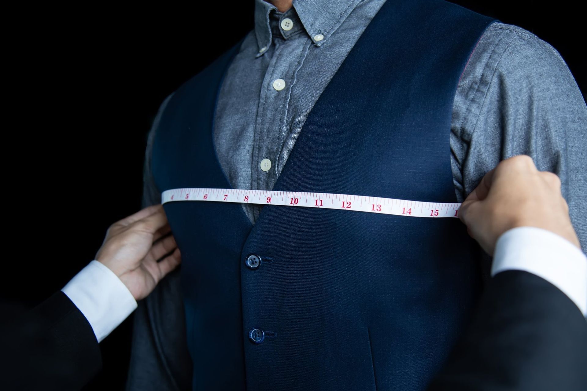Tailor measuring a man’s navy vest with a tape measure over a blue shirt
