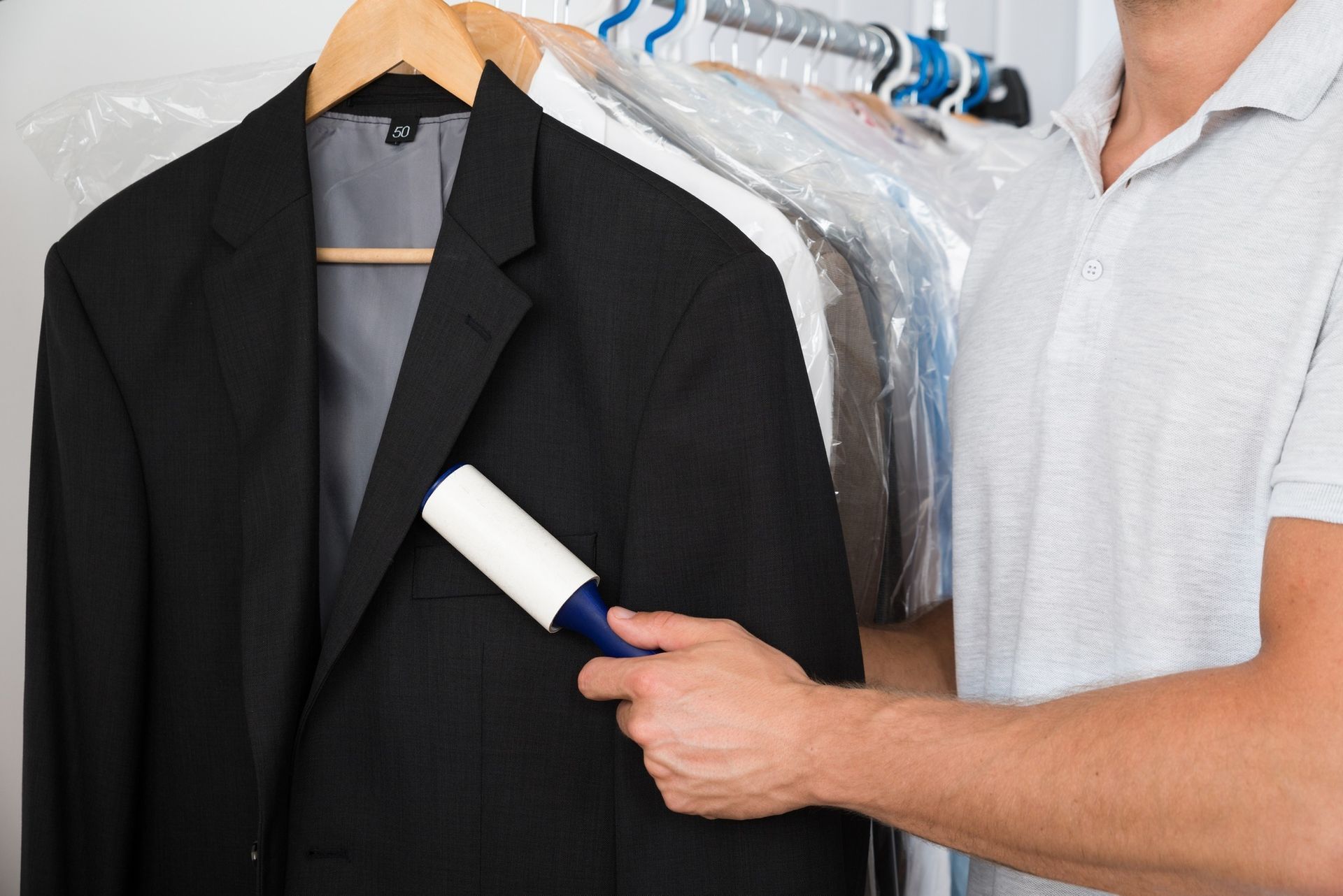 Person using a lint roller on a black suit jacket in a closet with hanging clothes