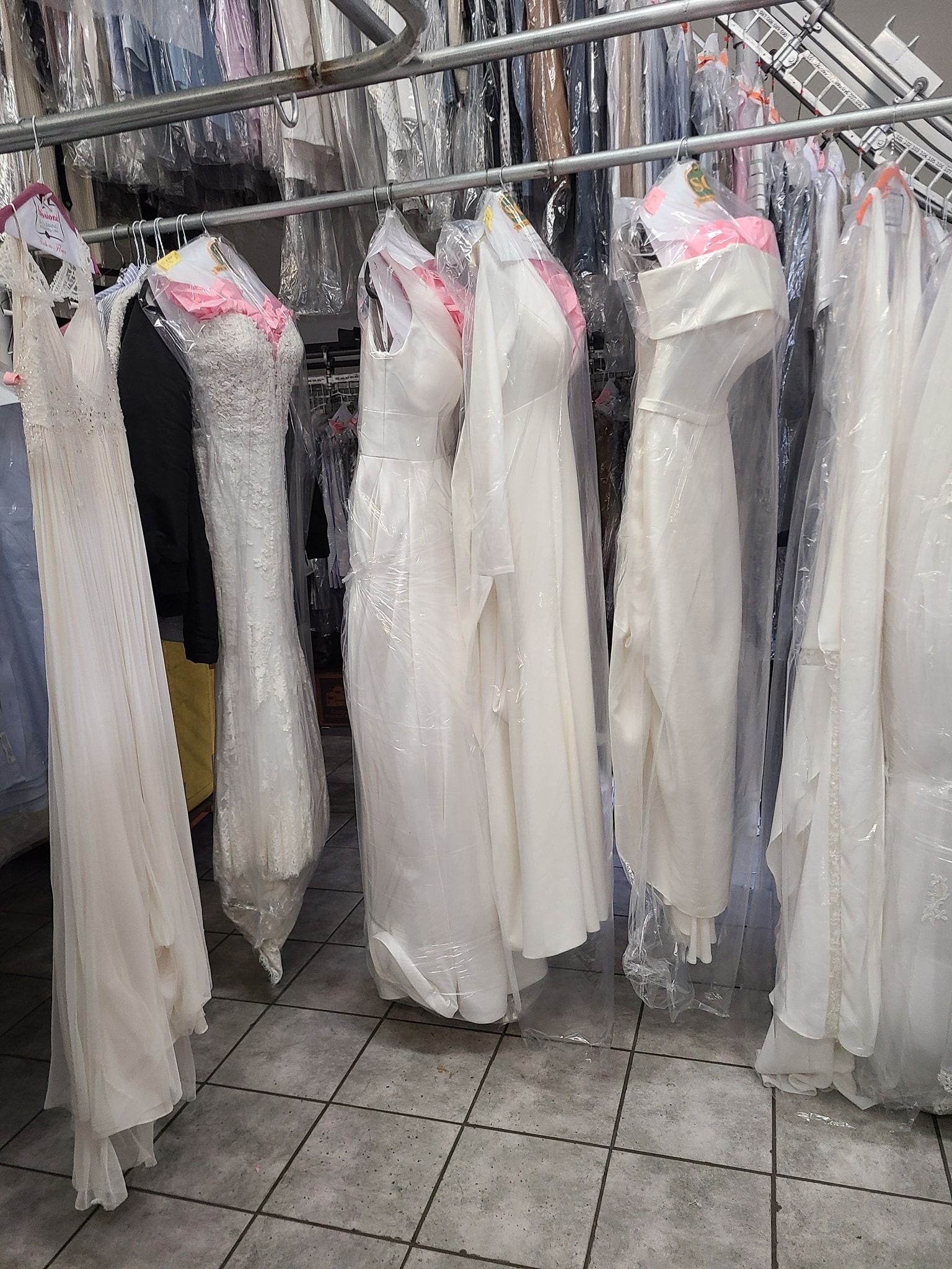 Racks of white dresses in garment bags hanging in a clothing store or alteration shop