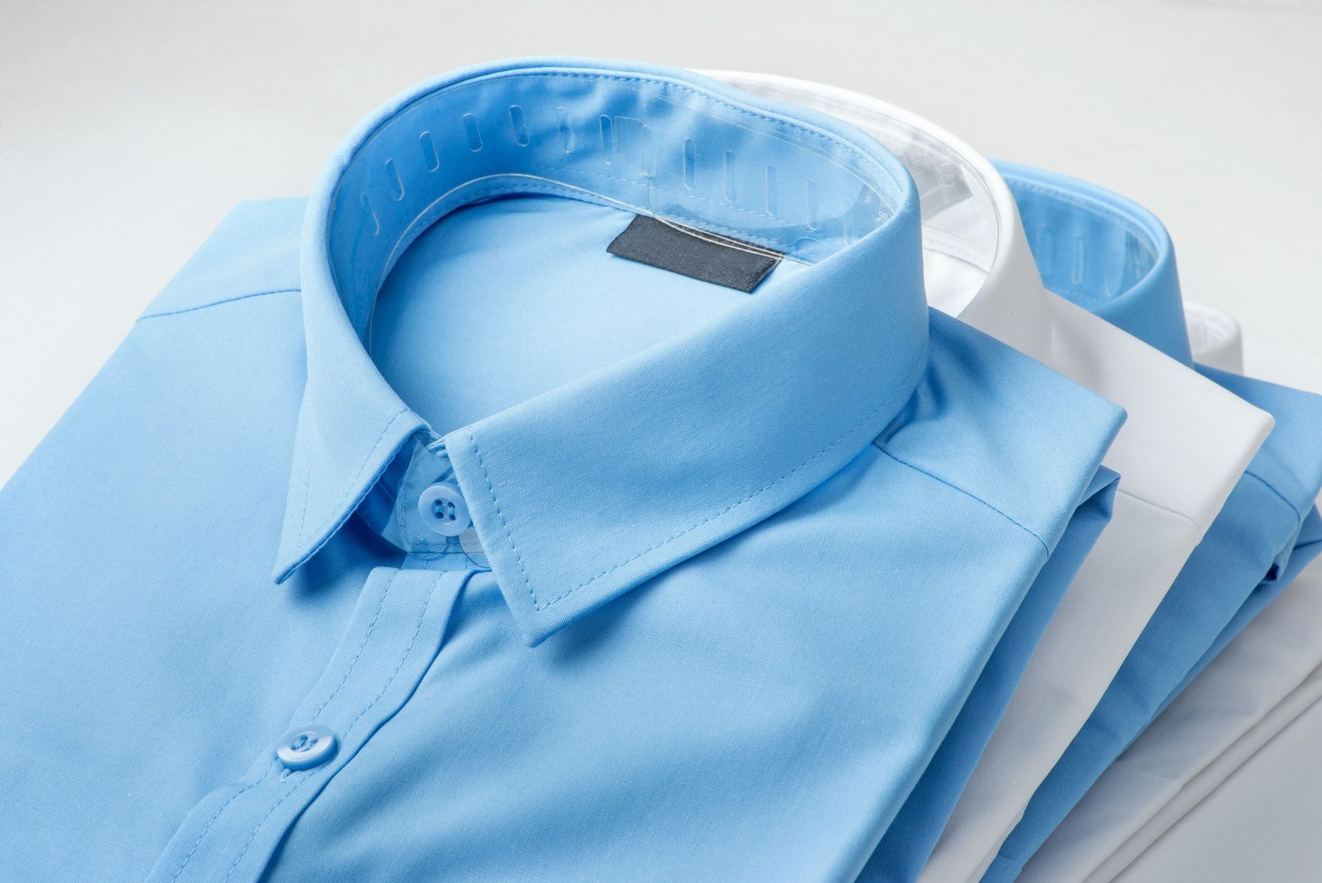Stacked folded blue dress shirts with collars visible