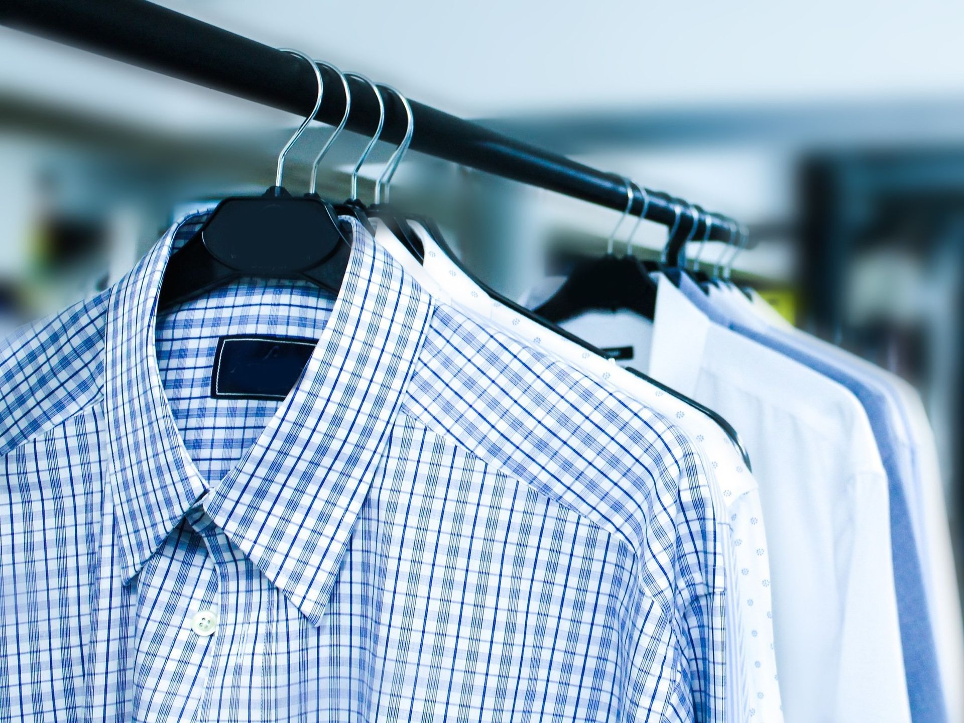 Plaid and white dress shirts hanging on a clothing rack in a store.