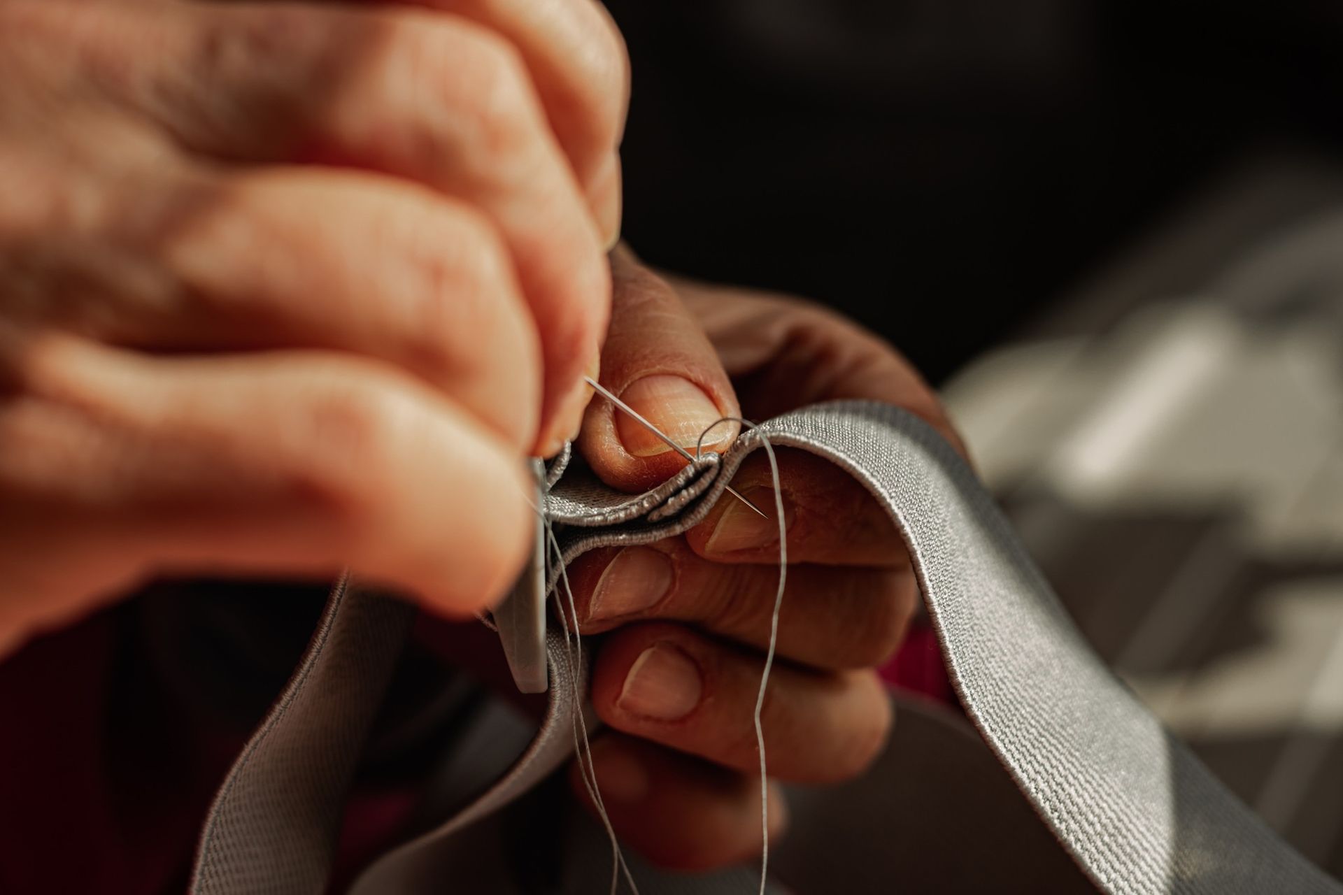Hands stitching gray fabric with thread and needle close-up
