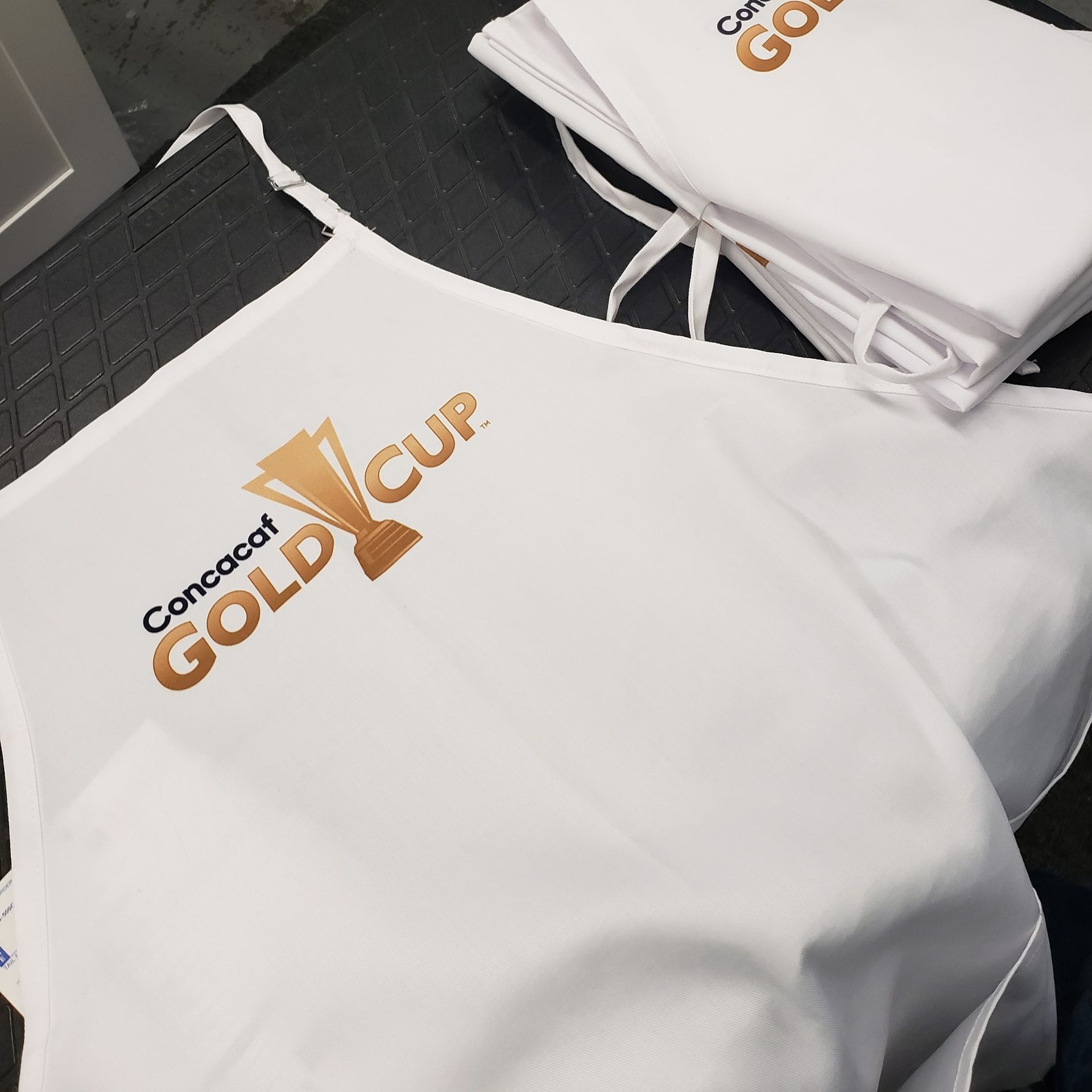 White shirts with gold “Concept GOLD Cup” logos laid out on a table.