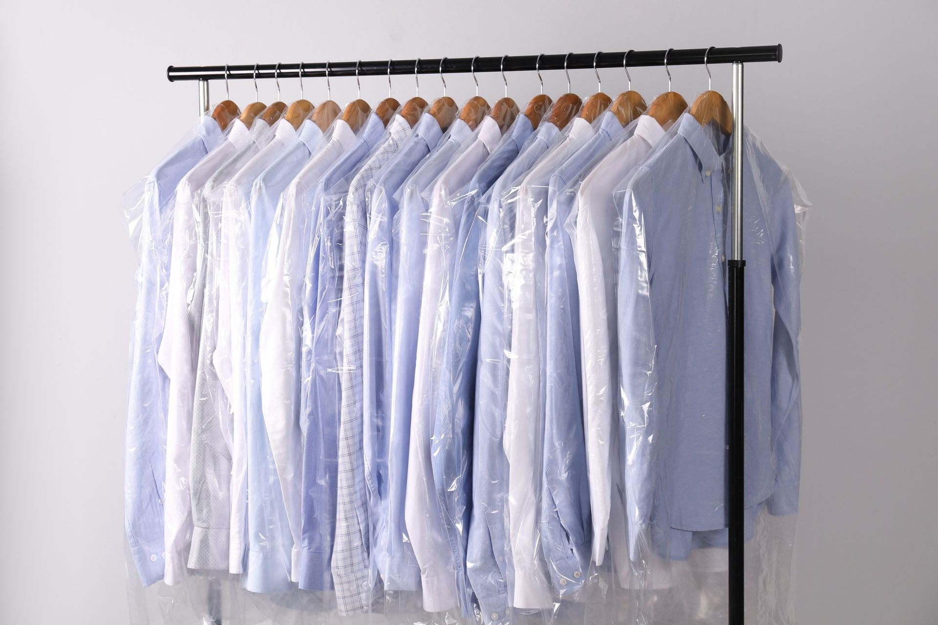 Row of white dress shirts hanging on wooden hangers on a black clothing rack