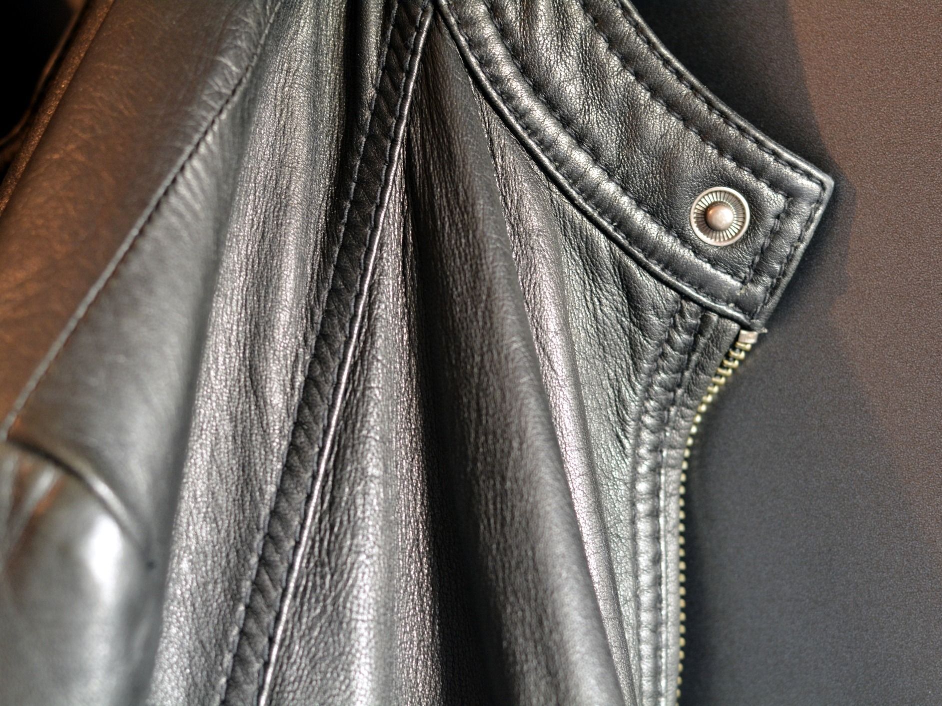 Close-up of a black leather jacket collar and zipper detail with a snap button