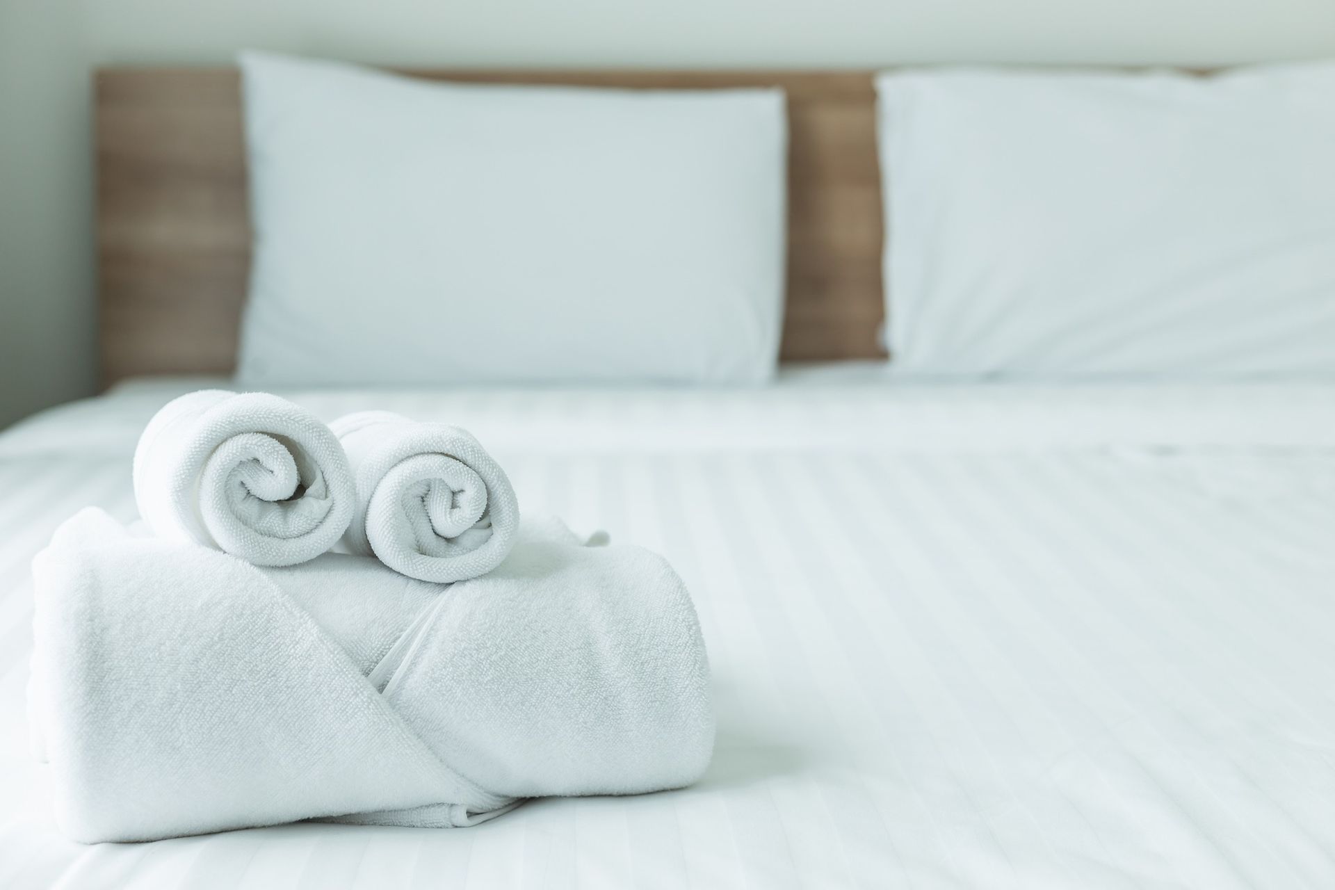 White towels rolled on a neatly made bed in a bright hotel room
