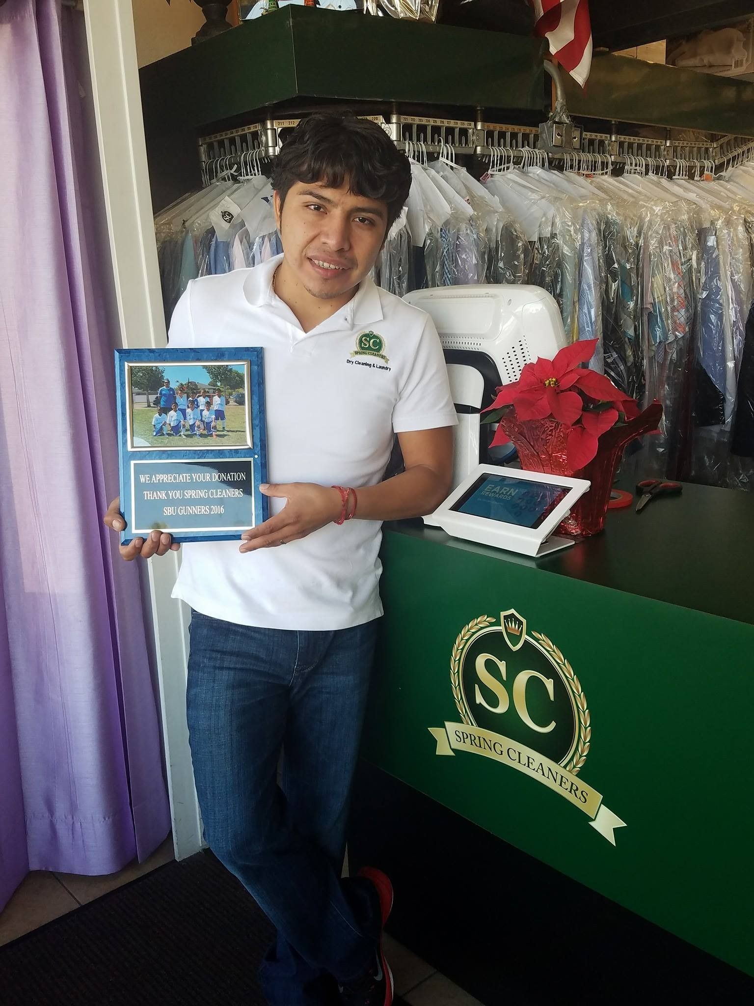Man holding a plaque in front of a green table with a red floral arrangement and framed display.