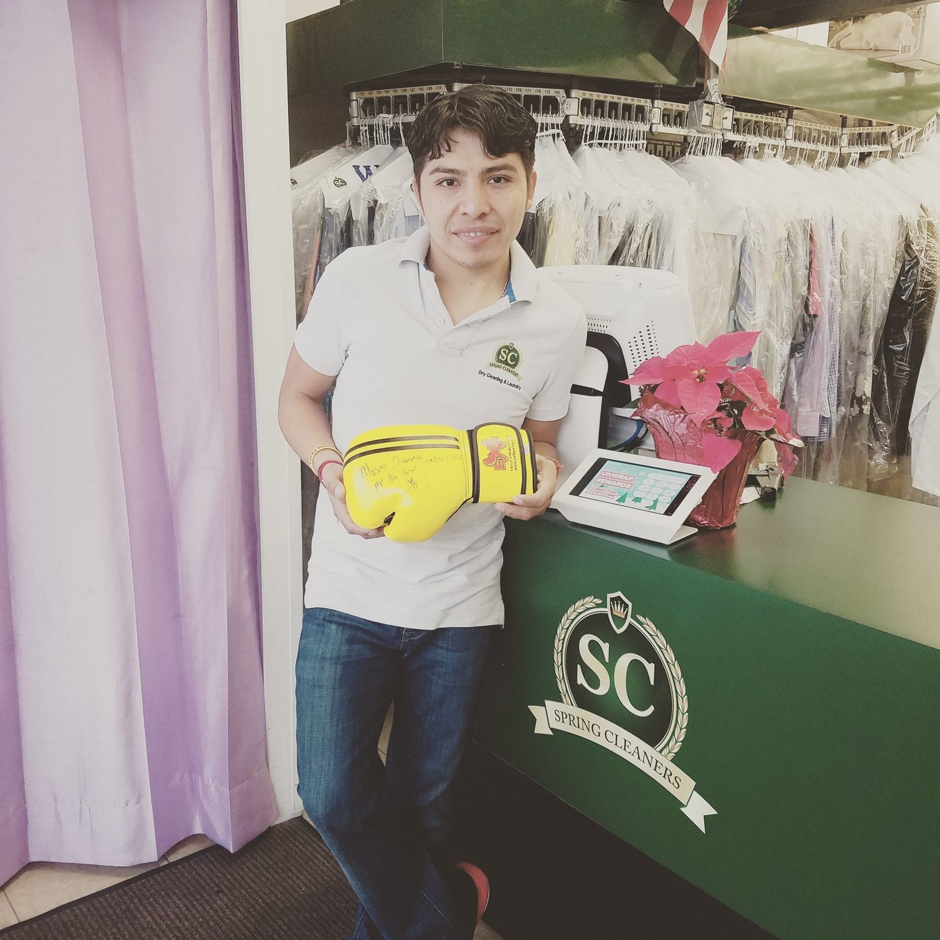 Person leaning at a counter, holding a yellow bag, in a clothing store with white garments and pink flowers.