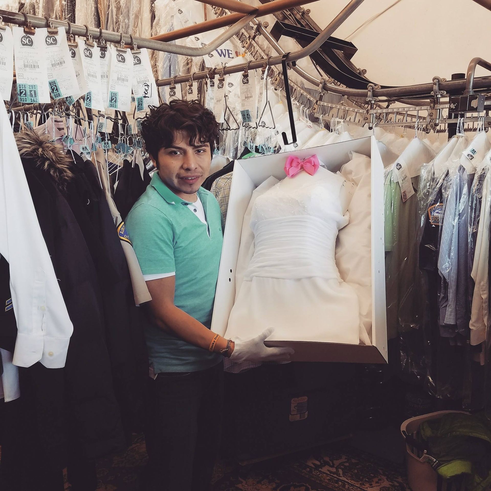 Person holding a framed white dress in a clothing shop, surrounded by hanging garments.
