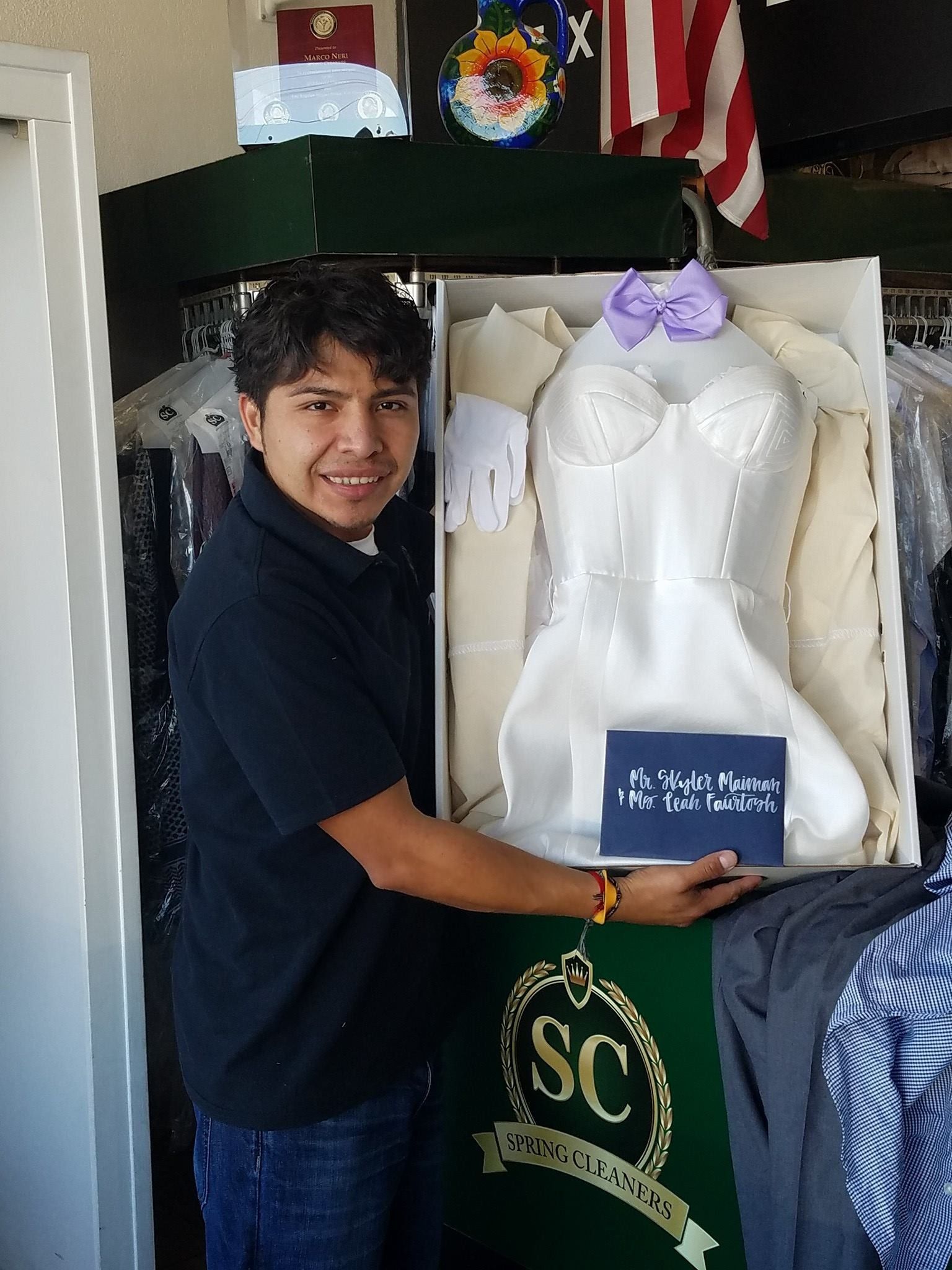 Person smiling beside a dress form in a room, holding a small blue sign.