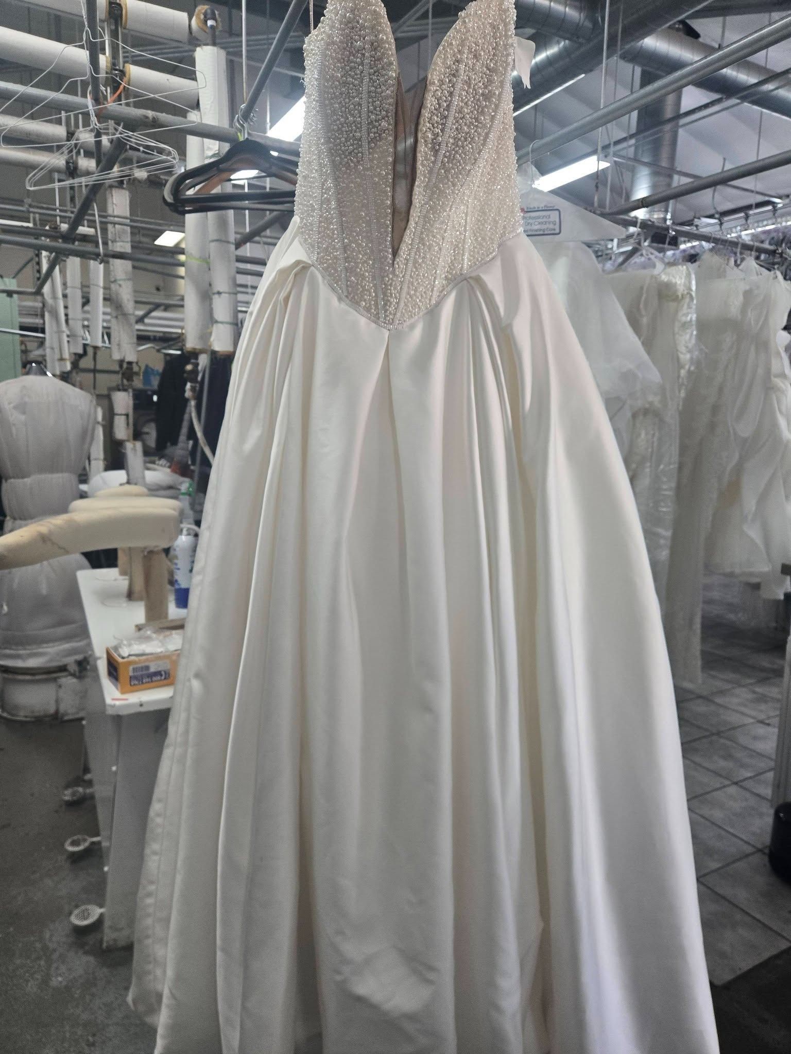 White satin wedding dress with a beaded, plunging bodice hanging in a bridal shop
