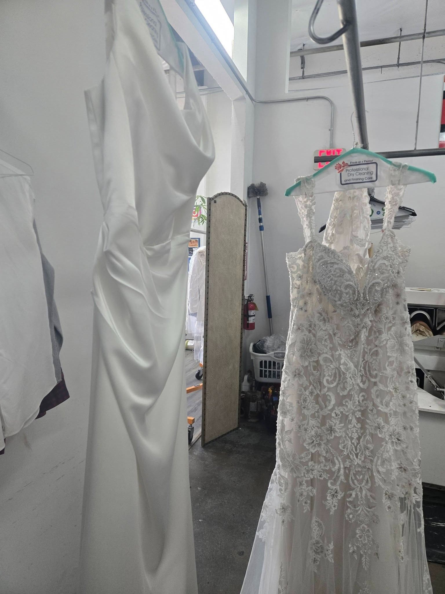 White lace wedding dress on a hanger in a clothing shop, beside a large white garment.