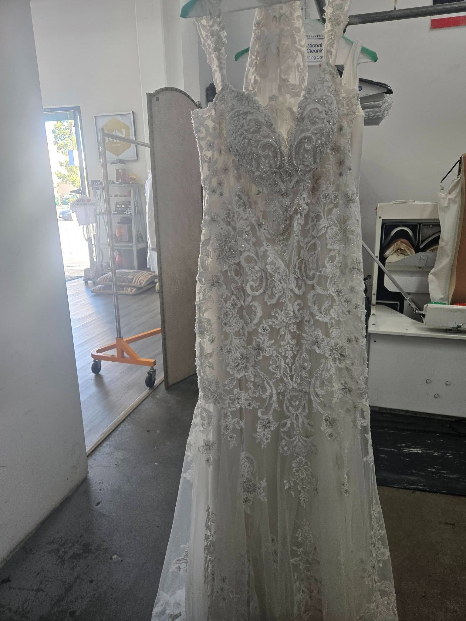 White lace wedding dress with beaded bodice hanging in a boutique or fitting room.