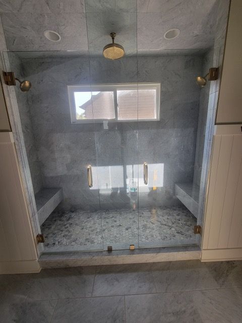 A bathroom with a walk in shower with a glass door and a window.