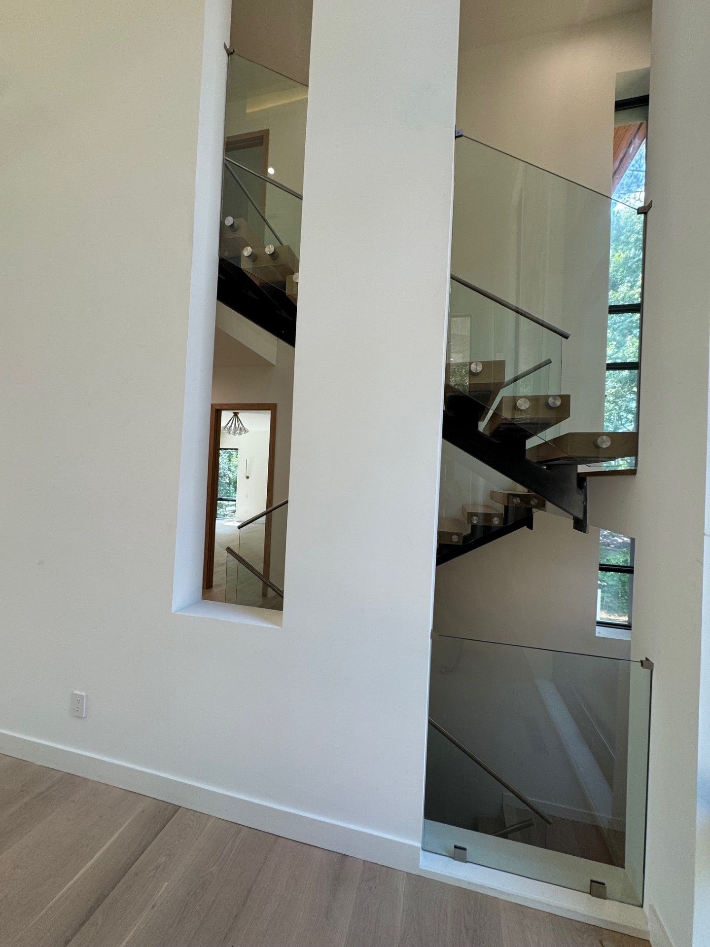Interior view of a modern staircase with glass railing and light wooden flooring