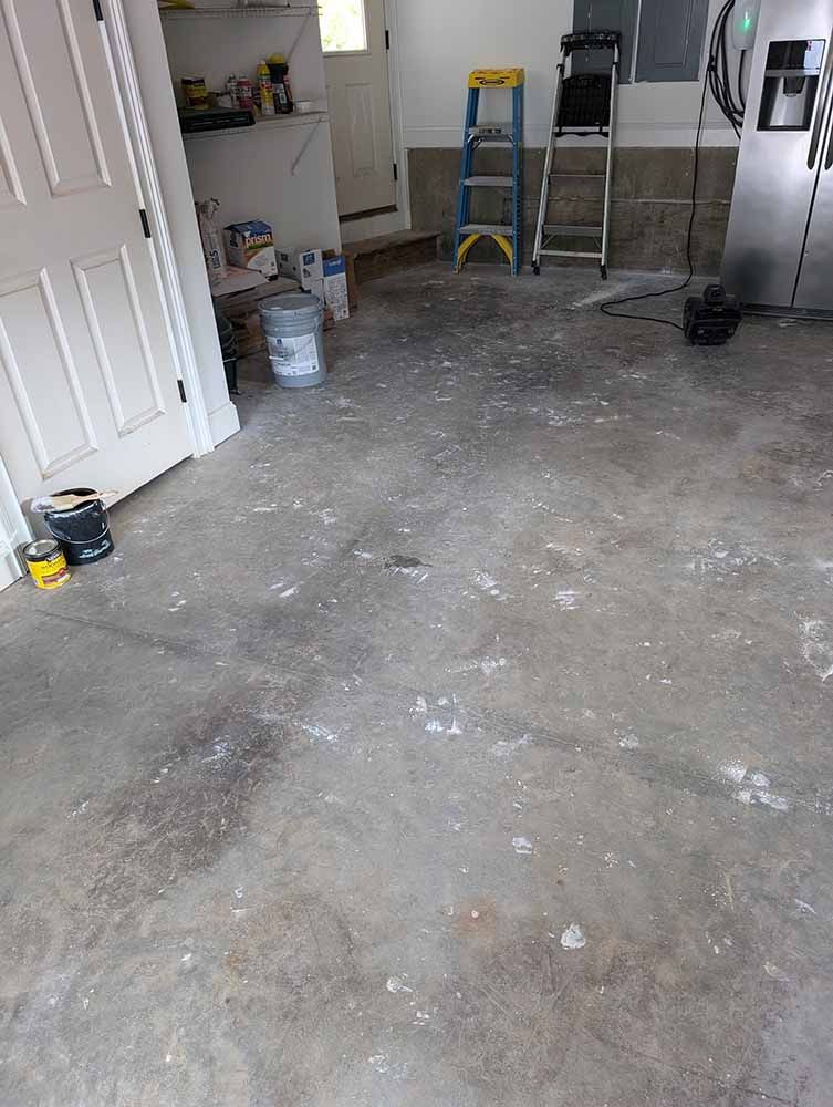 A dirty concrete floor in a garage with a ladder.