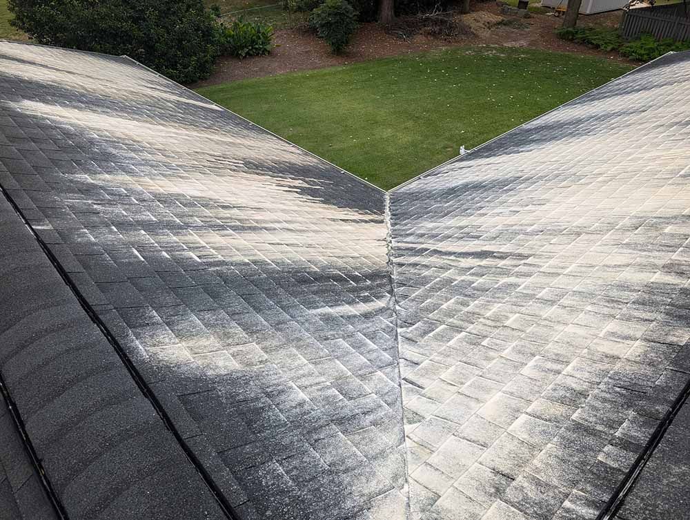 A roof with a lot of stains on it and a lawn in the background.