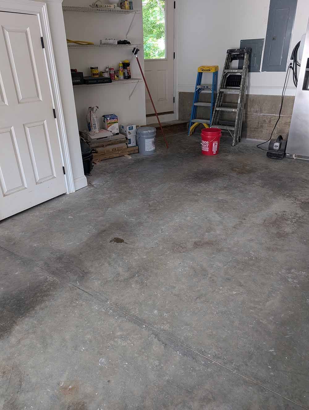 A garage with a ladder and buckets on the floor.