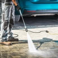 Person using a power washer to clean a driveway near a car.