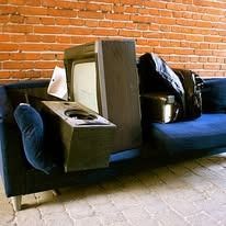 A vintage television and debris on a blue couch against a brick wall.