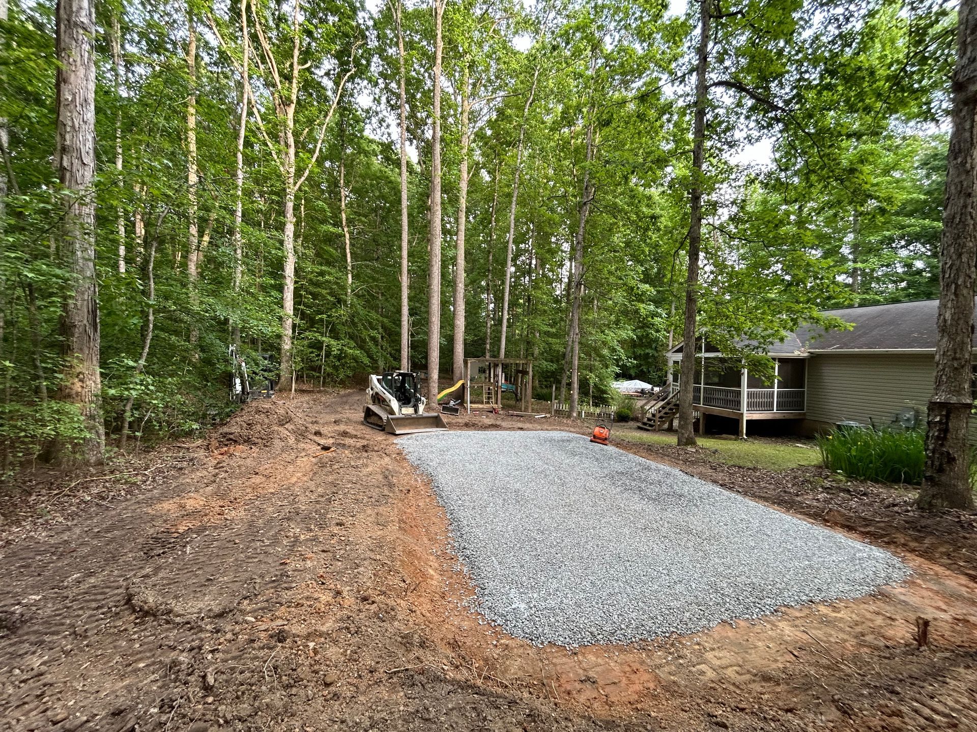 A gravel driveway is being built in the woods in front of a house.