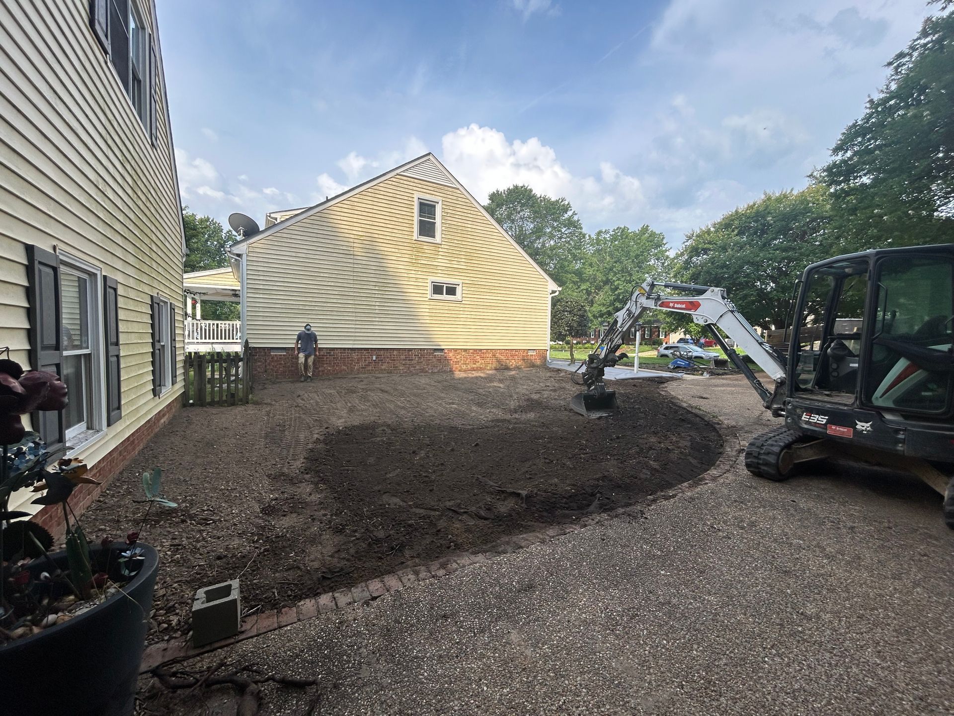 A large yellow house is being remodeled and a small excavator is sitting in front of it.