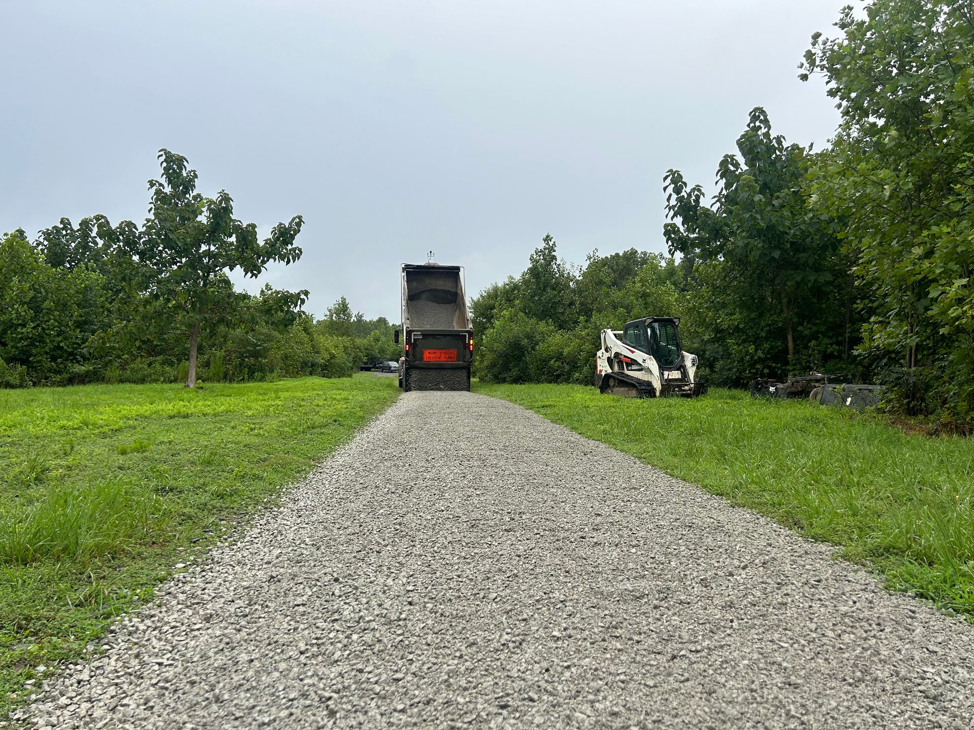 A dump truck is driving down a gravel road next to a tractor.